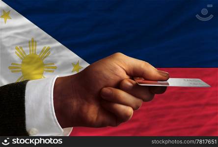 man stretching out credit card to buy goods in front of complete wavy national flag of philippines
