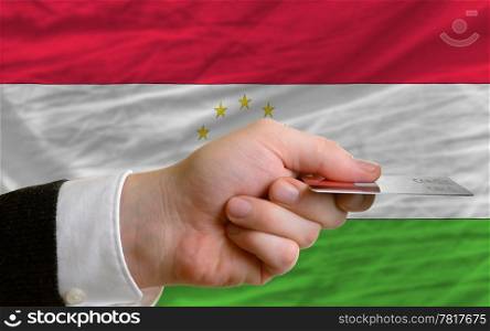 man stretching out credit card to buy goods in front of complete wavy national flag of tajikistan