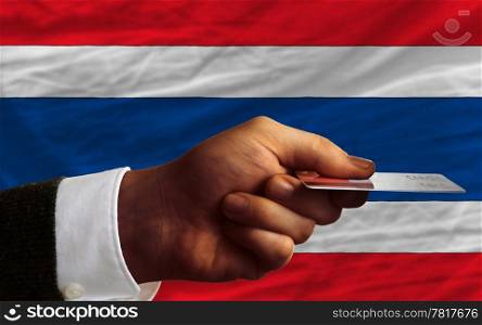 man stretching out credit card to buy goods in front of complete wavy national flag of thailand