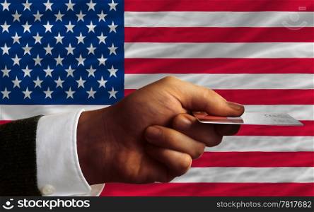 man stretching out credit card to buy goods in front of complete wavy national flag of united states of america