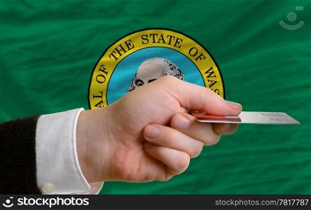 man stretching out credit card to buy goods in front of complete wavy national flag of american state of washington