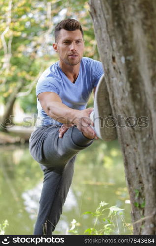 Man stretching out his leg against a tree