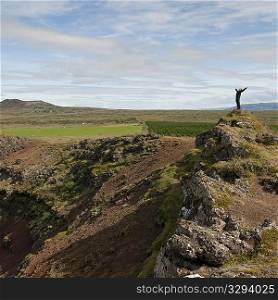 Man stretching with open arms on rocky hill outcrop above agricultural lands