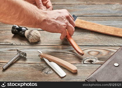 Man stropping straight razor with leather tool against old wooden background