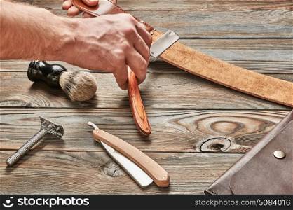 Man stropping straight razor with leather tool. Man stropping straight razor with leather tool against old wooden background