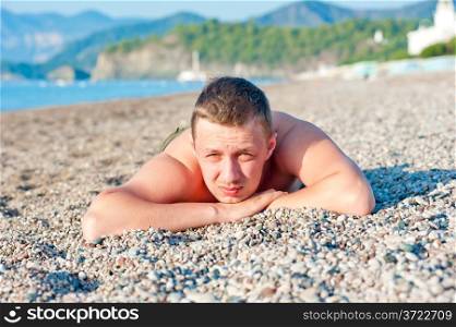 man sunbathes lying on a rocky beach