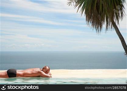 Man sunbathing at edge of pool ocean in background