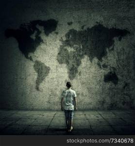 Man surrounded by limitations, daily routine, looking at the world map on a concrete wall. International travel cocept.