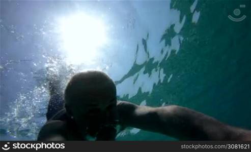 Man swimming underwater, free diving and holding GoPro video camera. Leisure, summer fun, recreation, holiday, vacations, water sport in Mediterannean Sea, Italy