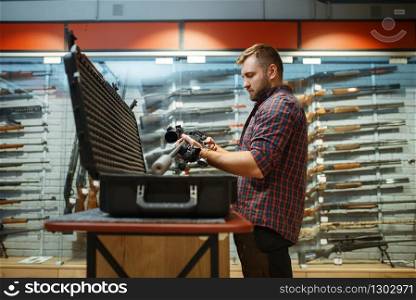 Man takes sniper rifle from the case in gun shop. Euqipment for hunters on stand in weapon store, hunting and sport shooting hobby. Man takes sniper rifle from the case in gun shop