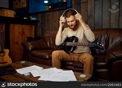 Man taking off headphones finish music lesson. Guy sitting with guitar at home studio. Man taking off headphones finish music lesson