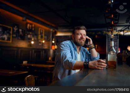 Man talking by mobile phone at the counter in bar. One male person resting in pub, human emotions, leisure activities, nightlife. Man talking by mobile phone at the counter in bar