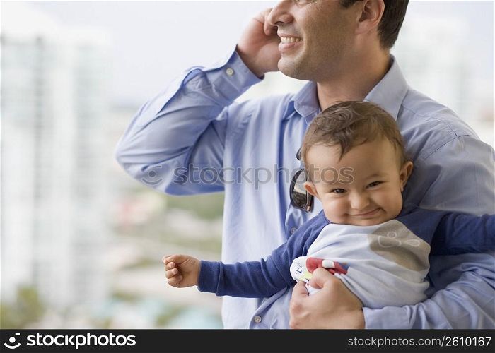 Man talking on a mobile phone and holding his son