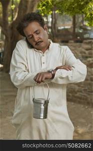 Man talking on cell phone and holding milk canister looking at watch