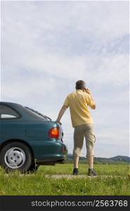 Man talking on cell phone beside his car which has a breakdown or a empty fuel tank