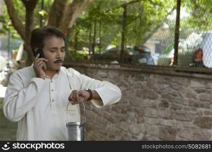 Man talking on cell phone holding milk canister and looking at watch