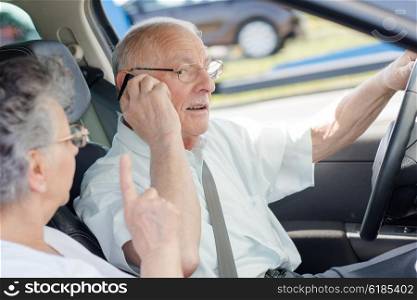 Man talking on telephone while driving, being reprimanded by wife