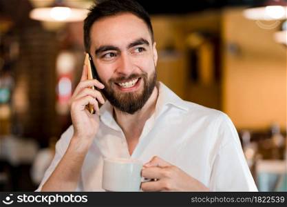 Man talking on the phone while drinking a cup of coffee at a coffee shop.