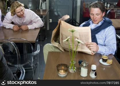 man talking to his neighbour customer who is reading a newspaper in a restaurant
