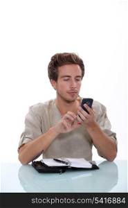 Man texting on his cellphone with an open diary on a white desk
