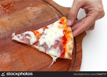 Man took last one slice of delicious Italian pizza. In frame hand taking slice of hot pizza with ham on wooden board on white table. Pizza time. Side view. Close-up
