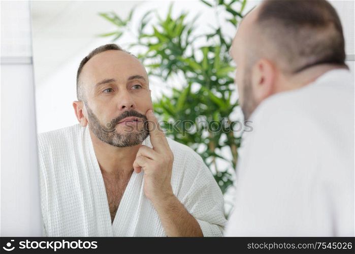 man touching beard and face looking in mirror