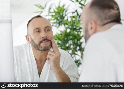 man touching beard and face looking in mirror
