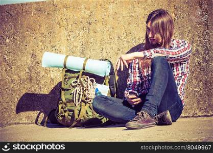 Man tourist backpacker outdoor sitting by grunge wall using mobile phone. Internet, tourism. Young hipster guy tramping