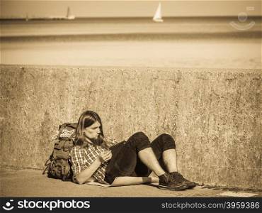 Man tourist backpacker relaxing outdoor sitting by grunge wall using tablet. Internet, tourism active lifestyle. Young hipster guy tramping