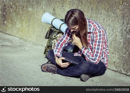 Man tourist backpacker relaxing outdoor sitting by grunge wall using tablet. Internet, tourism active lifestyle. Young hipster guy tramping