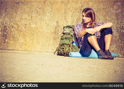 Man tourist backpacker relaxing outdoor sitting tired by grunge wall. Adventure, summer, tourism active lifestyle. Young hipster guy tramping
