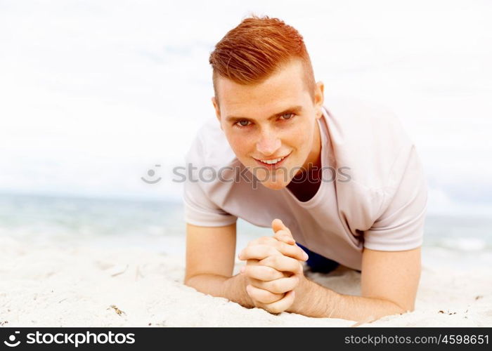 Man training on beach outside. Handsome caucasian male doing exercises on beach