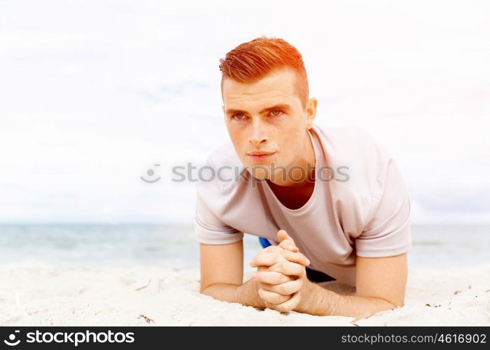 Man training on beach outside. Handsome caucasian male doing exercises on beach