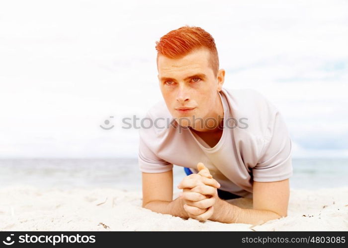 Man training on beach outside. Handsome caucasian male doing exercises on beach