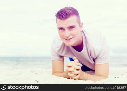 Man training on beach outside. Handsome caucasian male doing exercises on beach