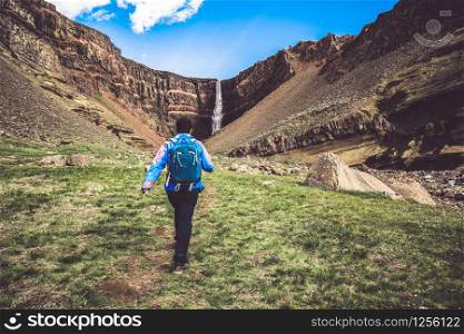 Man traveler hiking in Icelandic summer landscape at the Hengifoss waterfall in Iceland. The waterfall is situated in the eastern part of Iceland.