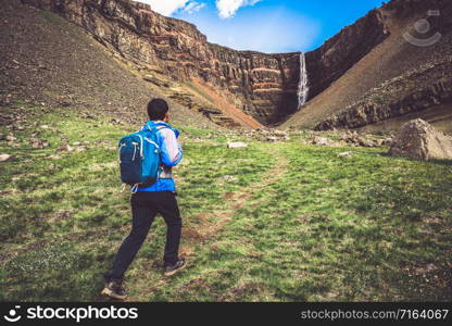 Man traveler hiking in Icelandic summer landscape at the Hengifoss waterfall in Iceland. The waterfall is situated in the eastern part of Iceland.