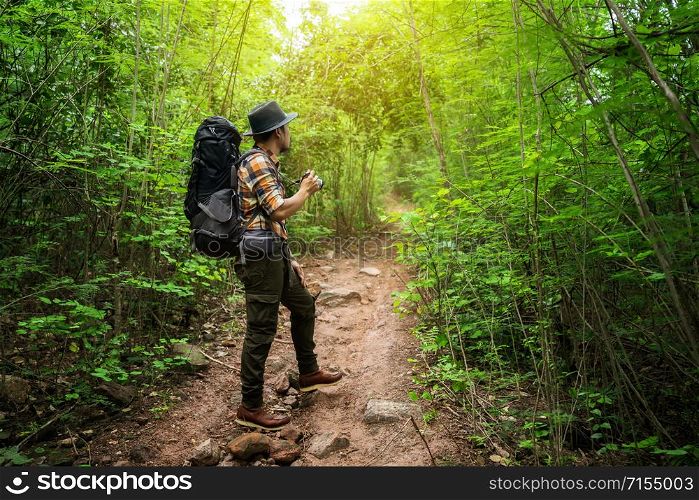 man traveler holding camera with backpack standing in the natural forest
