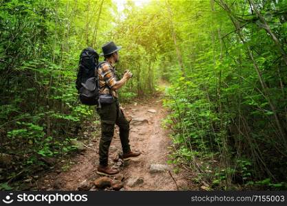 man traveler holding camera with backpack standing in the natural forest