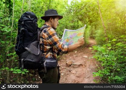 man traveler with backpack and map searching directions in the natural forest