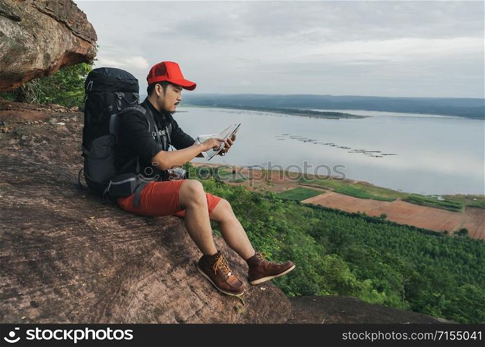 man traveler with backpack looking at the map on the edge of cliff, on a top of the rock mountain