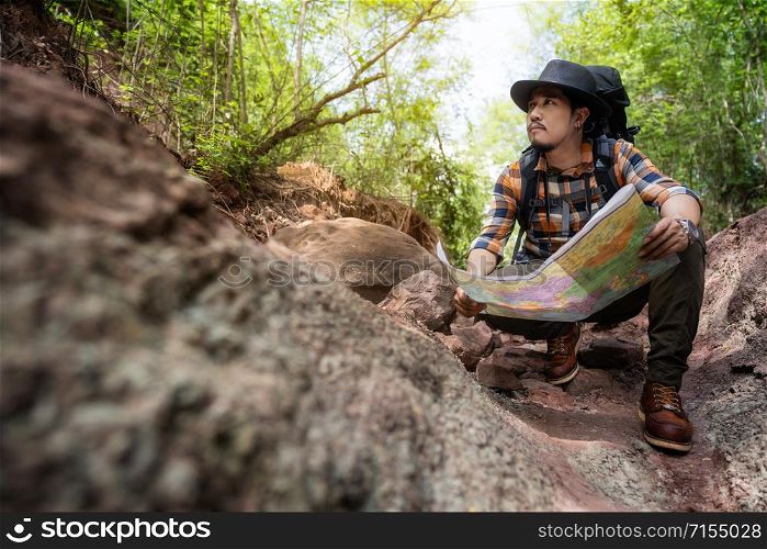 man traveler with backpack sitting and reading map in the natural forest