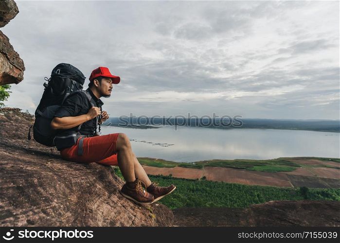 man traveler with backpack sitting on the edge of cliff, on a top of the rock mountain