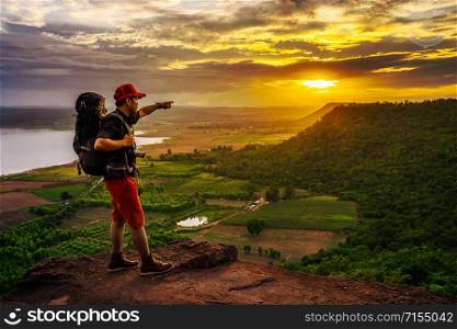 man traveler with backpack standing on the edge of cliff, on a top of the rock mountain at sunset