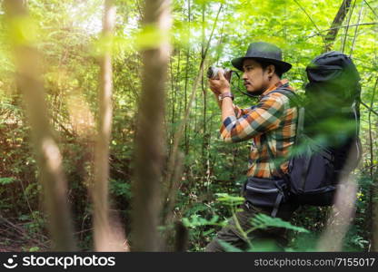 man traveler with backpack using camera to take a photo in the natural forest