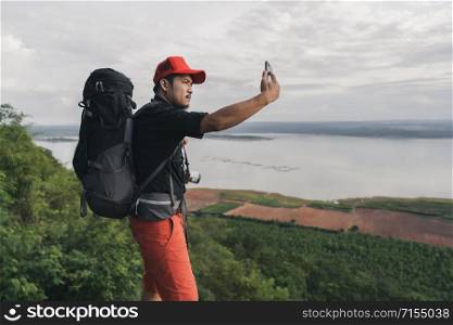 man traveler with backpack using smartphone take a selfie on the edge of cliff, on a top of the rock mountain