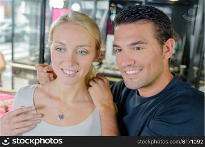 Man trying heart shaped necklace on girlfriend