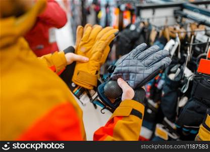 Man trying on gloves for ski or snowboarding, sports shop. Winter season extreme lifestyle, active leisure store, male customer with protect equipment. Man trying on gloves for ski or snowboarding
