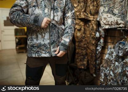 Man trying on uniform at showcase in gun shop. Euqipment and rifles for hunters on stand in weapon store, hunting and sport shooting hobby. Man trying on uniform at showcase in gun shop