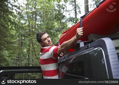 Man tying kayak on car roof, in forest